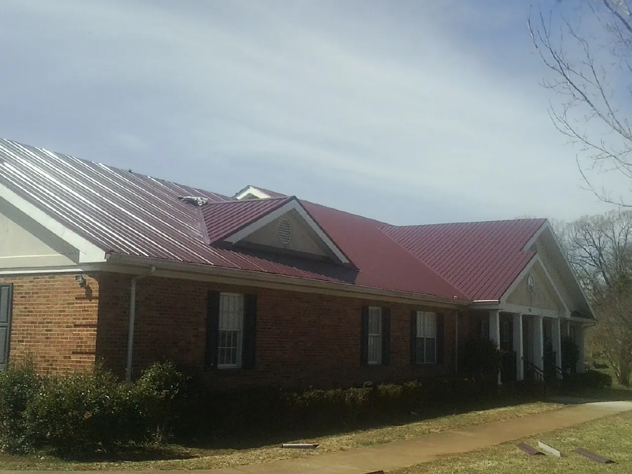Red metal roof with gabled entries on a long brick building, from a Hail Damage Roof Repair job in Mogadore
