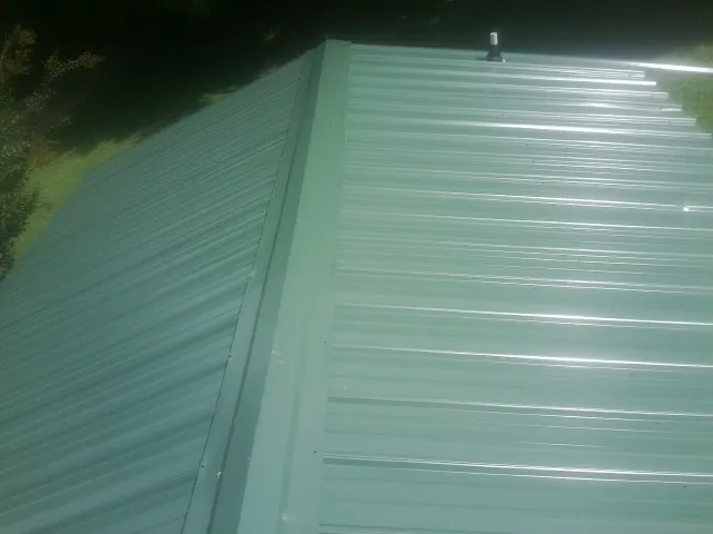 New green metal panels meeting at the ridge of a roof — Flat Roof Repair work by our crew in Mogadore