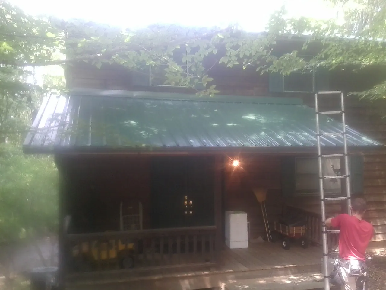 Worker on a ladder at the green porch roof of a wooded cabin in Mogadore
