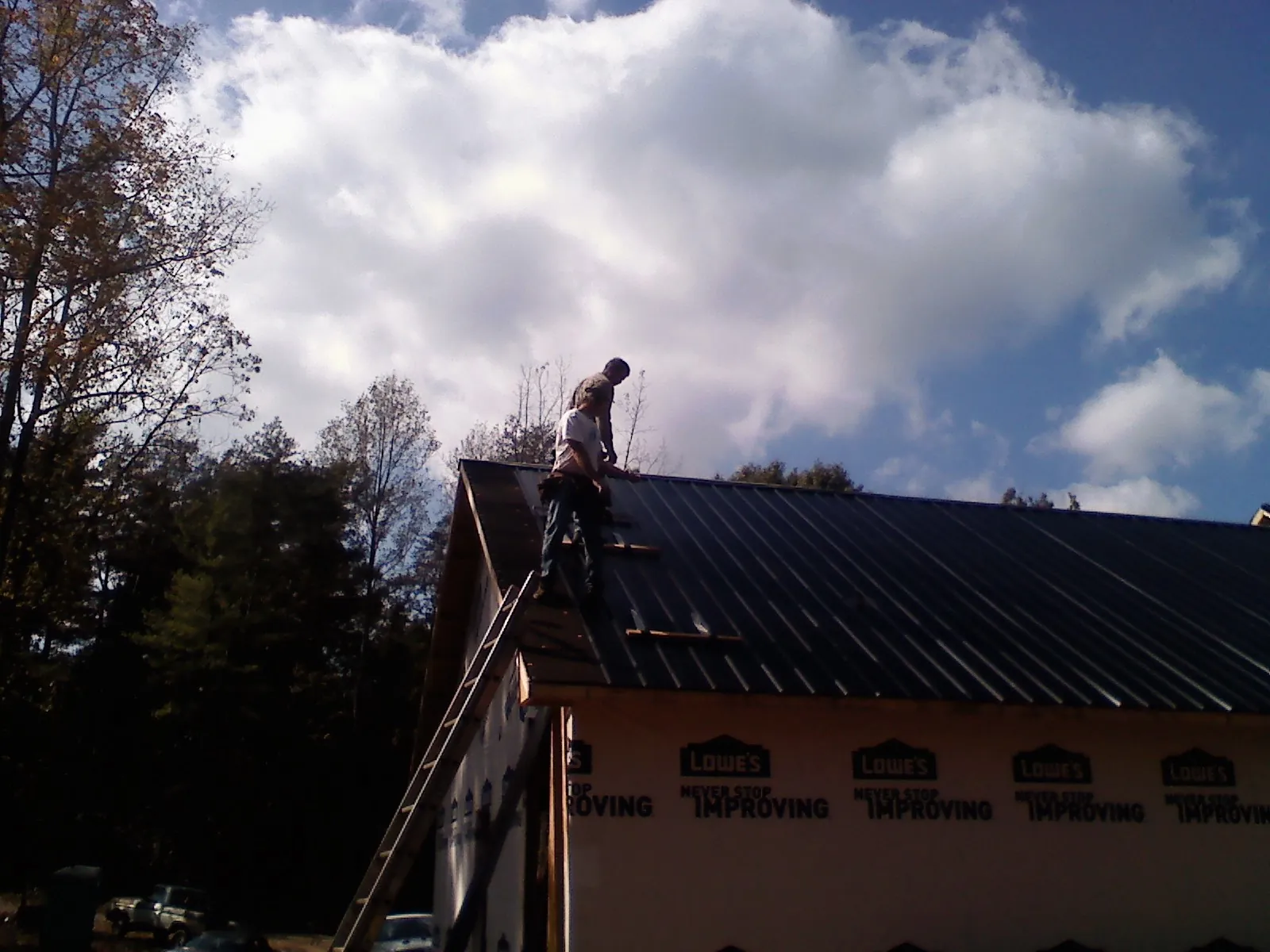 Roofer fastening dark metal panels high against a cloudy sky, from a Roof Inspection job in Mogadore