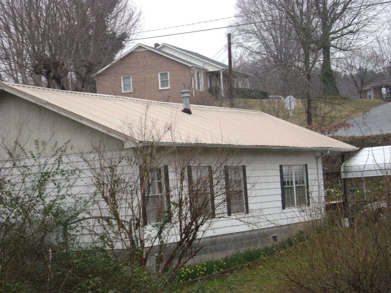 Tan metal roof on a white sided house set into a hillside — Commercial Roofing by Roofing Brothers in Mogadore